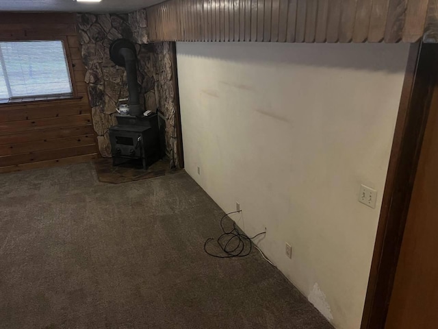 unfurnished living room featuring carpet flooring, a wood stove, and wooden walls