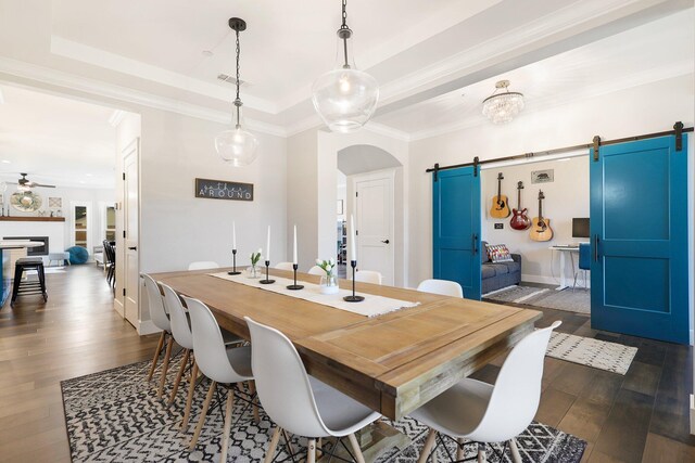 dining room with ceiling fan, a raised ceiling, dark hardwood / wood-style floors, a barn door, and crown molding