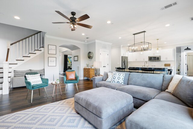 living room featuring ceiling fan with notable chandelier, sink, dark wood-type flooring, and ornamental molding