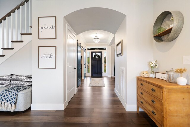 corridor with a barn door, dark wood-type flooring, and ornamental molding