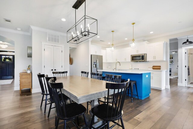 dining area with sink, crown molding, a notable chandelier, and dark hardwood / wood-style flooring