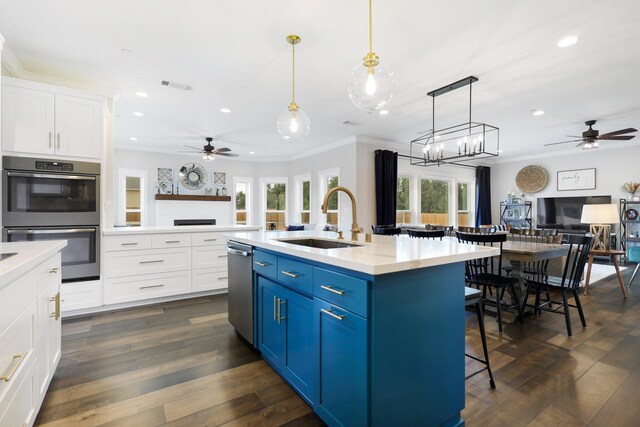 kitchen featuring dark wood-type flooring, hanging light fixtures, blue cabinets, appliances with stainless steel finishes, and sink