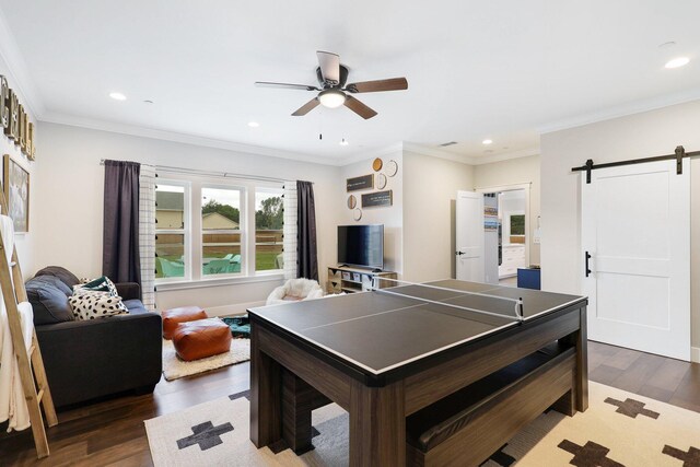 recreation room with ceiling fan, a barn door, ornamental molding, and dark hardwood / wood-style flooring