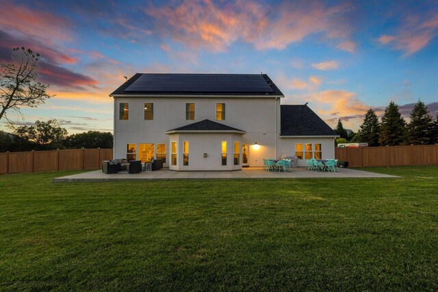 back house at dusk featuring an outdoor living space, solar panels, a patio area, and a yard