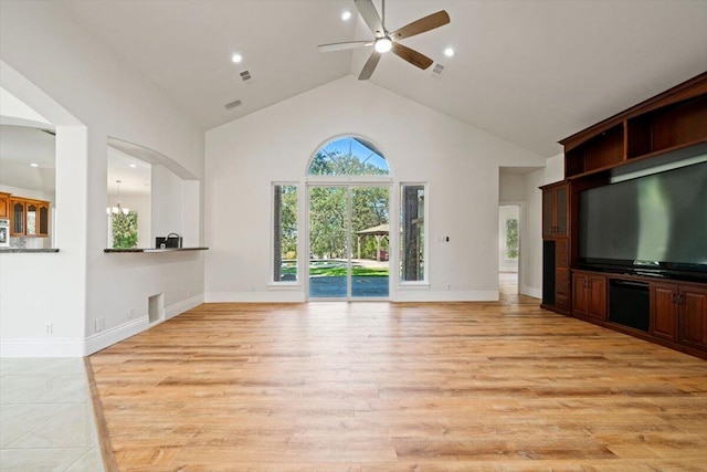 unfurnished living room featuring ceiling fan with notable chandelier, high vaulted ceiling, and light hardwood / wood-style flooring