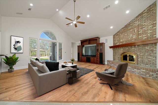 living room featuring a fireplace, light hardwood / wood-style floors, high vaulted ceiling, and ceiling fan