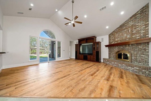 unfurnished living room with ceiling fan, light hardwood / wood-style flooring, high vaulted ceiling, and a brick fireplace