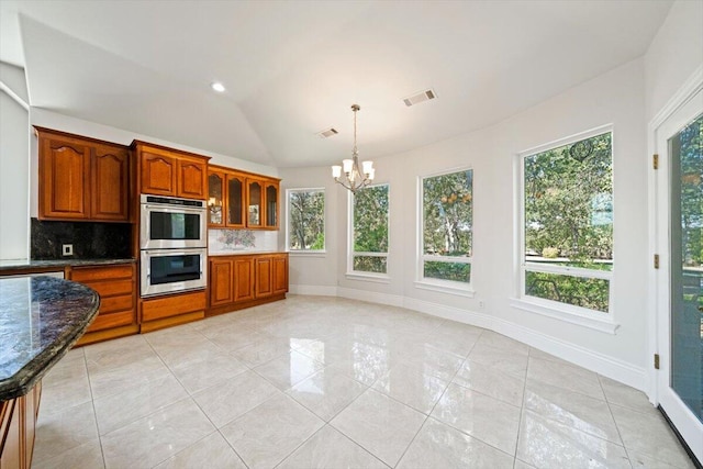 kitchen with lofted ceiling, backsplash, dark stone counters, hanging light fixtures, and stainless steel double oven