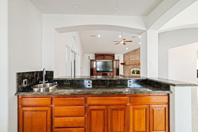 kitchen featuring a fireplace, vaulted ceiling, dark stone countertops, and sink