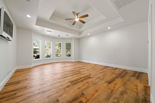 empty room with ceiling fan, light hardwood / wood-style floors, and a raised ceiling