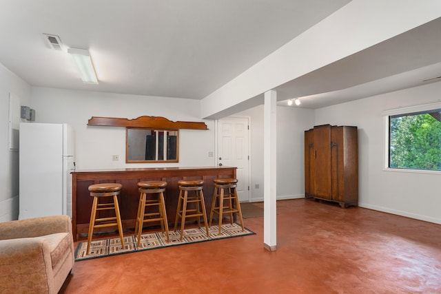 kitchen with a breakfast bar, kitchen peninsula, fridge, and concrete floors