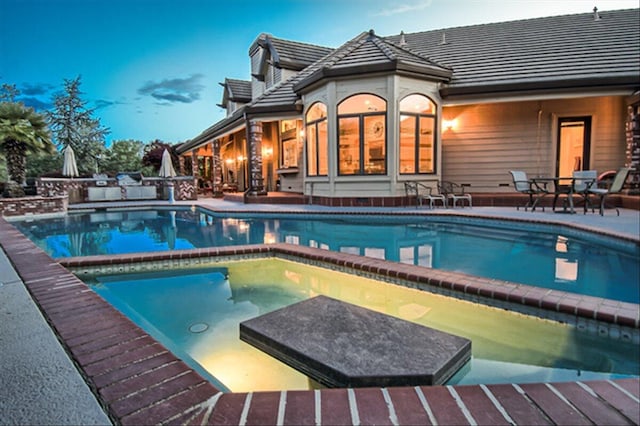 pool at dusk featuring an in ground hot tub and a patio area