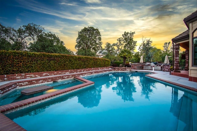 pool at dusk featuring an in ground hot tub and a patio