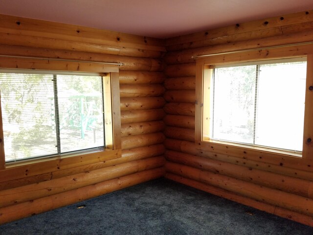 empty room with log walls, carpet, and a wealth of natural light