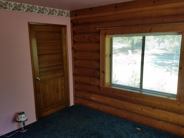 unfurnished bedroom with log walls, carpet flooring, and multiple windows