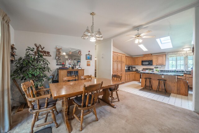 carpeted dining room featuring vaulted ceiling with skylight and ceiling fan with notable chandelier