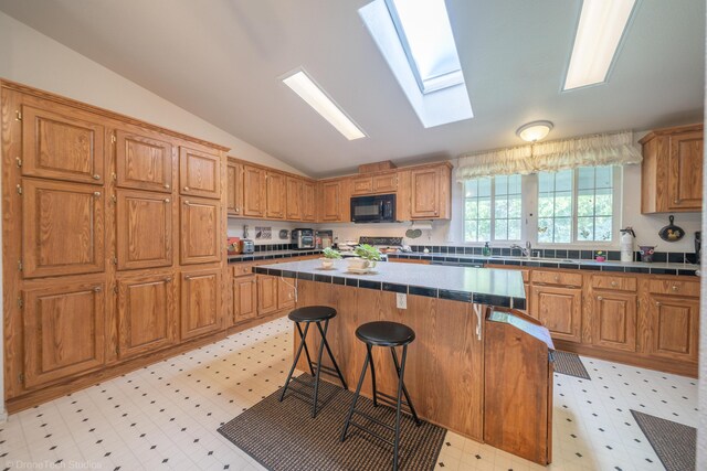 kitchen featuring tile countertops, a center island, lofted ceiling with skylight, and a breakfast bar