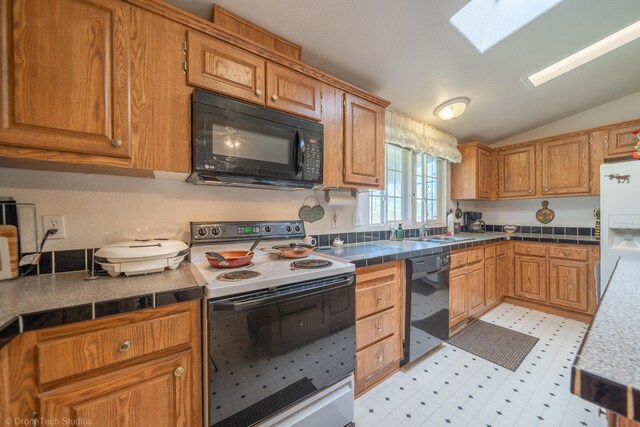 kitchen with black appliances, vaulted ceiling with skylight, sink, and tile countertops