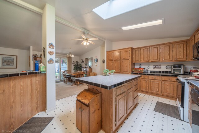 kitchen featuring a center island, tile countertops, vaulted ceiling with skylight, ceiling fan, and a kitchen bar