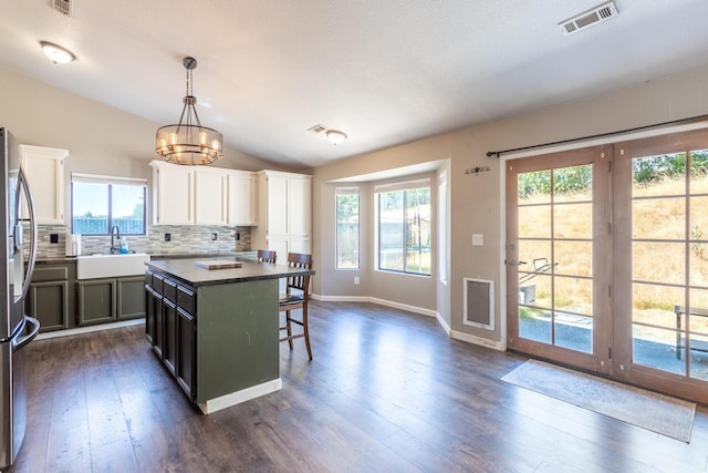 kitchen featuring lofted ceiling, dark wood-style flooring, a sink, visible vents, and decorative backsplash