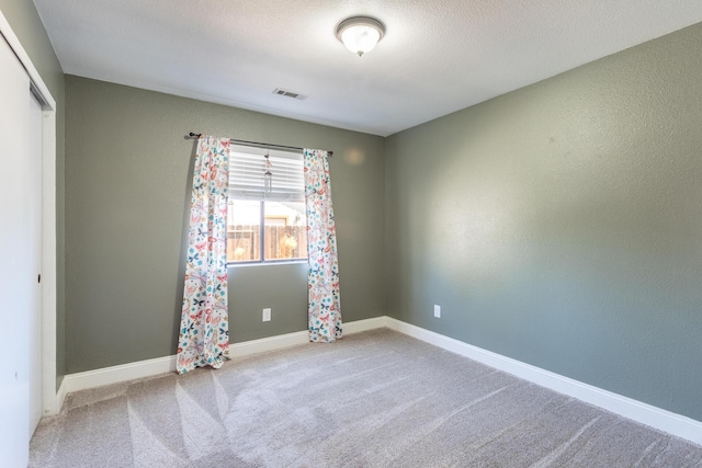 spare room featuring a textured ceiling, carpet floors, visible vents, and baseboards