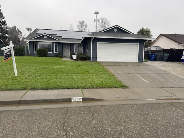 ranch-style home with concrete driveway, an attached garage, fence, roof mounted solar panels, and a front yard