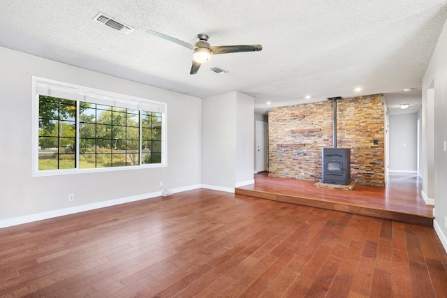 unfurnished living room featuring wood-type flooring, a textured ceiling, ceiling fan, and a wood stove