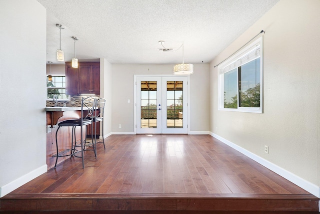 dining area featuring a textured ceiling, dark wood-type flooring, french doors, and plenty of natural light