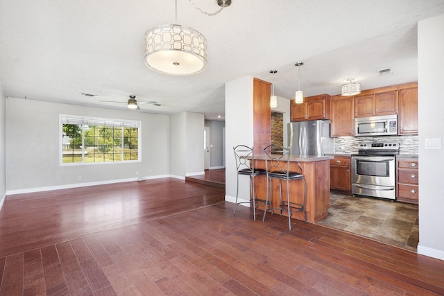 kitchen with a breakfast bar area, stainless steel appliances, hanging light fixtures, ceiling fan, and decorative backsplash