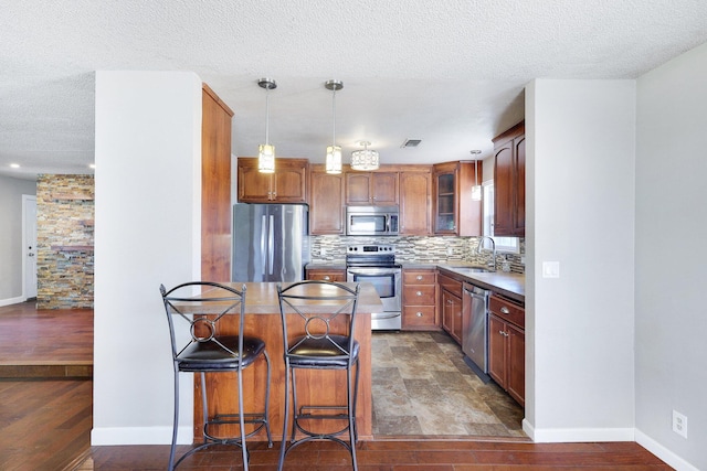 kitchen featuring decorative light fixtures, stainless steel appliances, a breakfast bar, tasteful backsplash, and sink