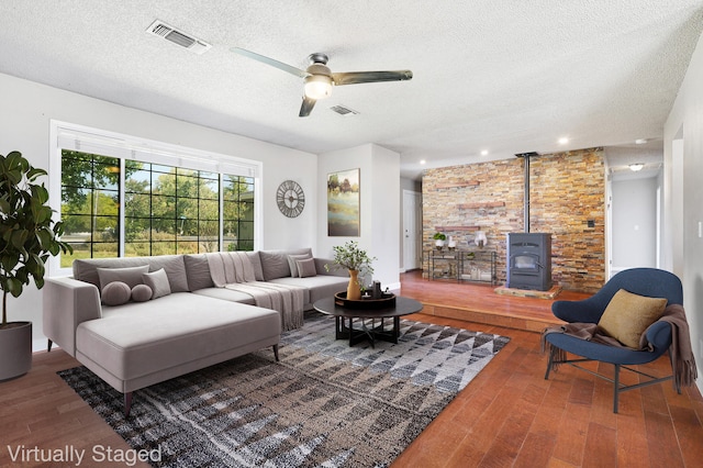 living room with hardwood / wood-style flooring, a textured ceiling, ceiling fan, and a wood stove