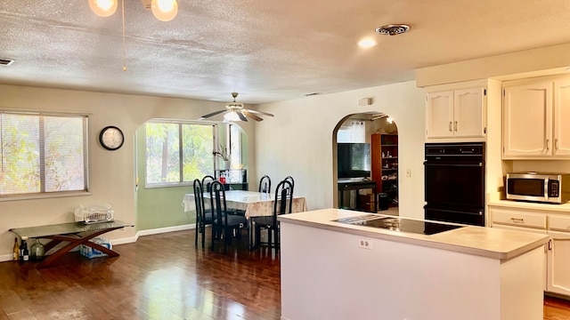 kitchen featuring dark hardwood / wood-style floors, black appliances, a center island, ceiling fan, and white cabinets