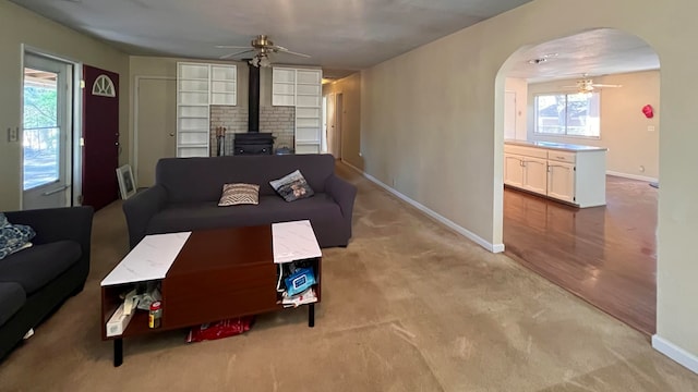 living room with a wood stove, light colored carpet, and ceiling fan