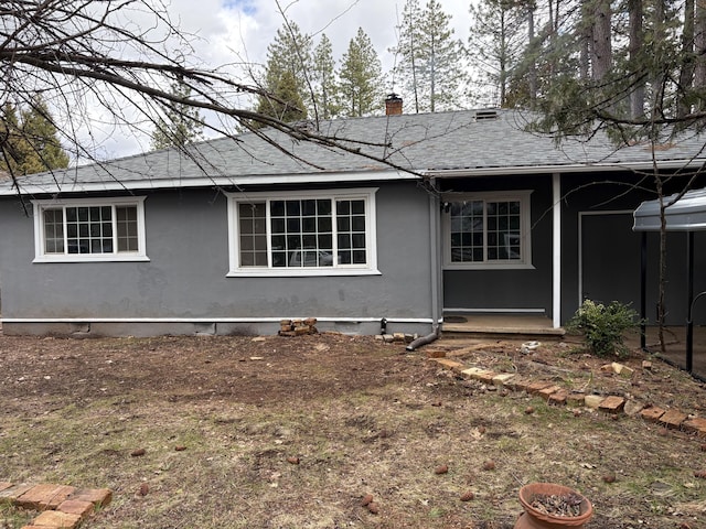 rear view of property featuring crawl space, stucco siding, a chimney, and roof with shingles