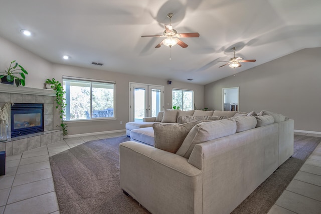 living room with a tiled fireplace, french doors, lofted ceiling, light tile patterned flooring, and ceiling fan