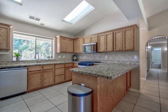 kitchen with vaulted ceiling with skylight, backsplash, stainless steel appliances, and sink