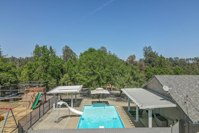 view of pool with a water slide, a patio, and a playground