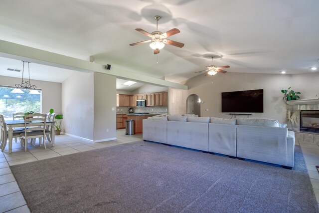 living room with a tiled fireplace, lofted ceiling, light colored carpet, and ceiling fan