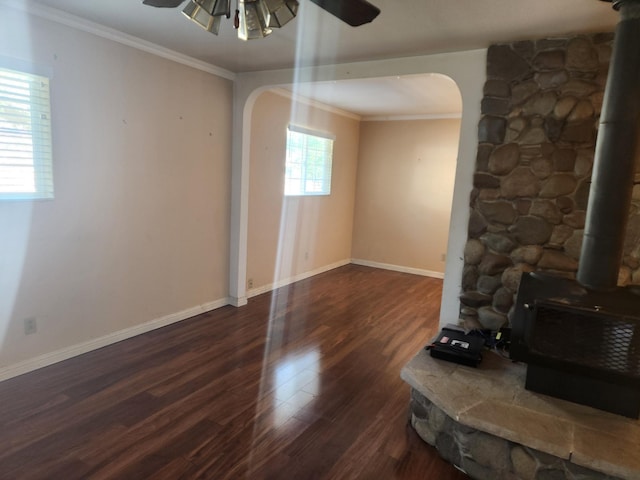 unfurnished living room featuring ceiling fan, a wood stove, dark hardwood / wood-style flooring, and ornamental molding