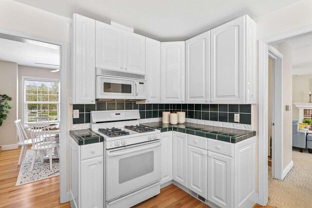 kitchen with white cabinetry, light wood-type flooring, white appliances, and tile countertops