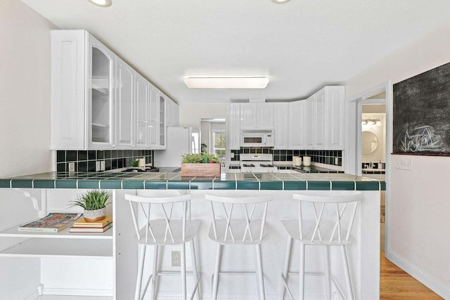 kitchen with white appliances, kitchen peninsula, tile counters, and white cabinetry