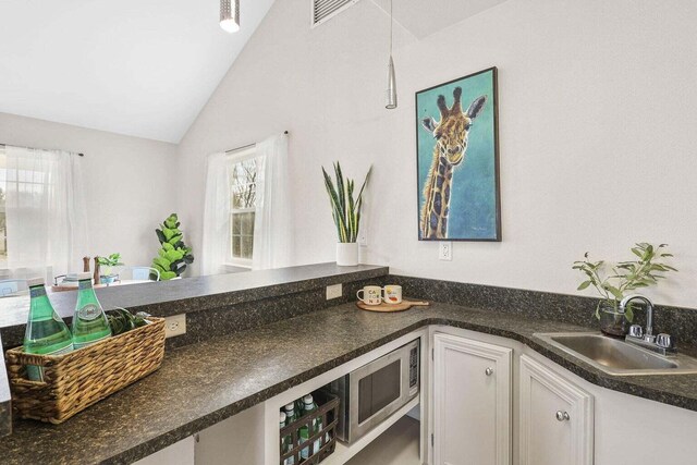 kitchen with white cabinets, vaulted ceiling, stainless steel microwave, and sink