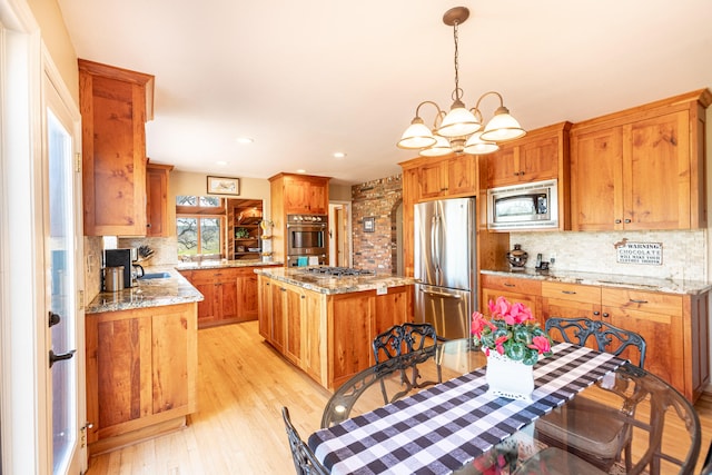 kitchen with a chandelier, backsplash, a center island, appliances with stainless steel finishes, and light hardwood / wood-style floors