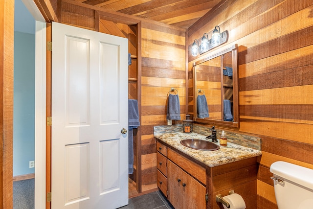 bathroom with tile patterned flooring, vanity, toilet, and wood walls