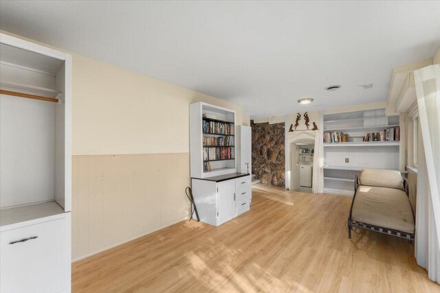 living room with light hardwood / wood-style flooring, built in shelves, and wooden walls