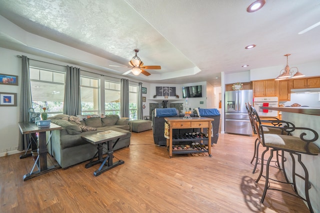 living room featuring a textured ceiling, a raised ceiling, ceiling fan, and light hardwood / wood-style flooring