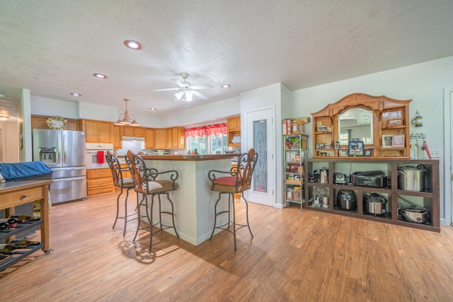 kitchen with hanging light fixtures, white oven, ceiling fan, light hardwood / wood-style flooring, and stainless steel refrigerator with ice dispenser