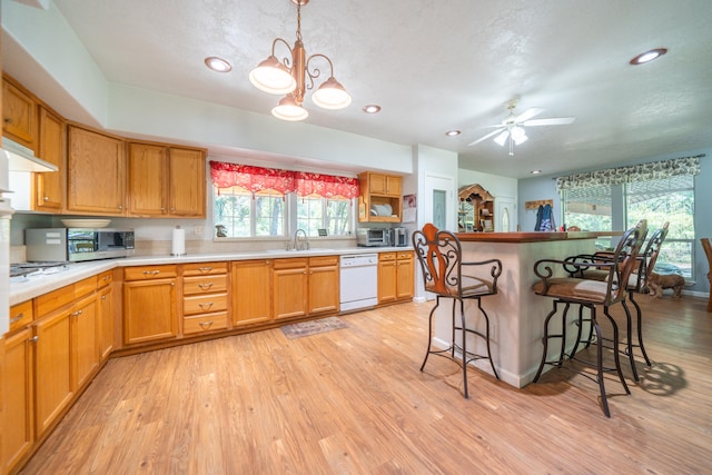 kitchen featuring a breakfast bar, ceiling fan with notable chandelier, dishwasher, pendant lighting, and light hardwood / wood-style flooring