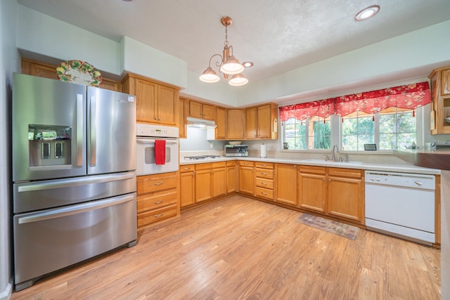 kitchen with hanging light fixtures, white appliances, light wood-type flooring, sink, and a chandelier