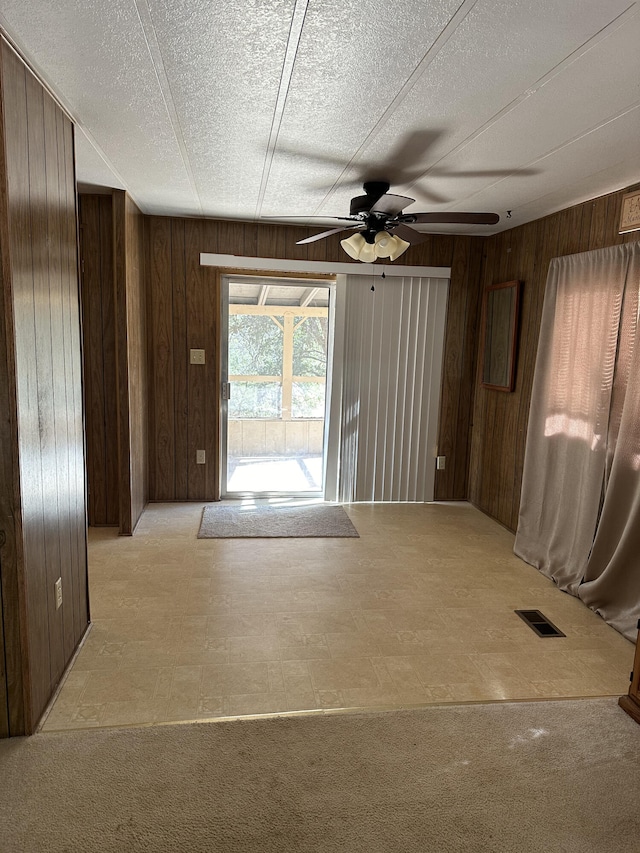 carpeted spare room with a textured ceiling, ceiling fan, and wooden walls